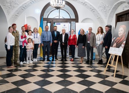 Fotografia. wernisaż wystawy piękno jedności w willi decjusza. w Holu głównym pod ścianami na sztalugach stoją fotografie. Goście wernisażu pozują do zdjęcia w rzędzie.